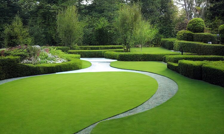 Välskött trädgård med grön gräsmatta, klippta häckar och med träd i bakgrunden.